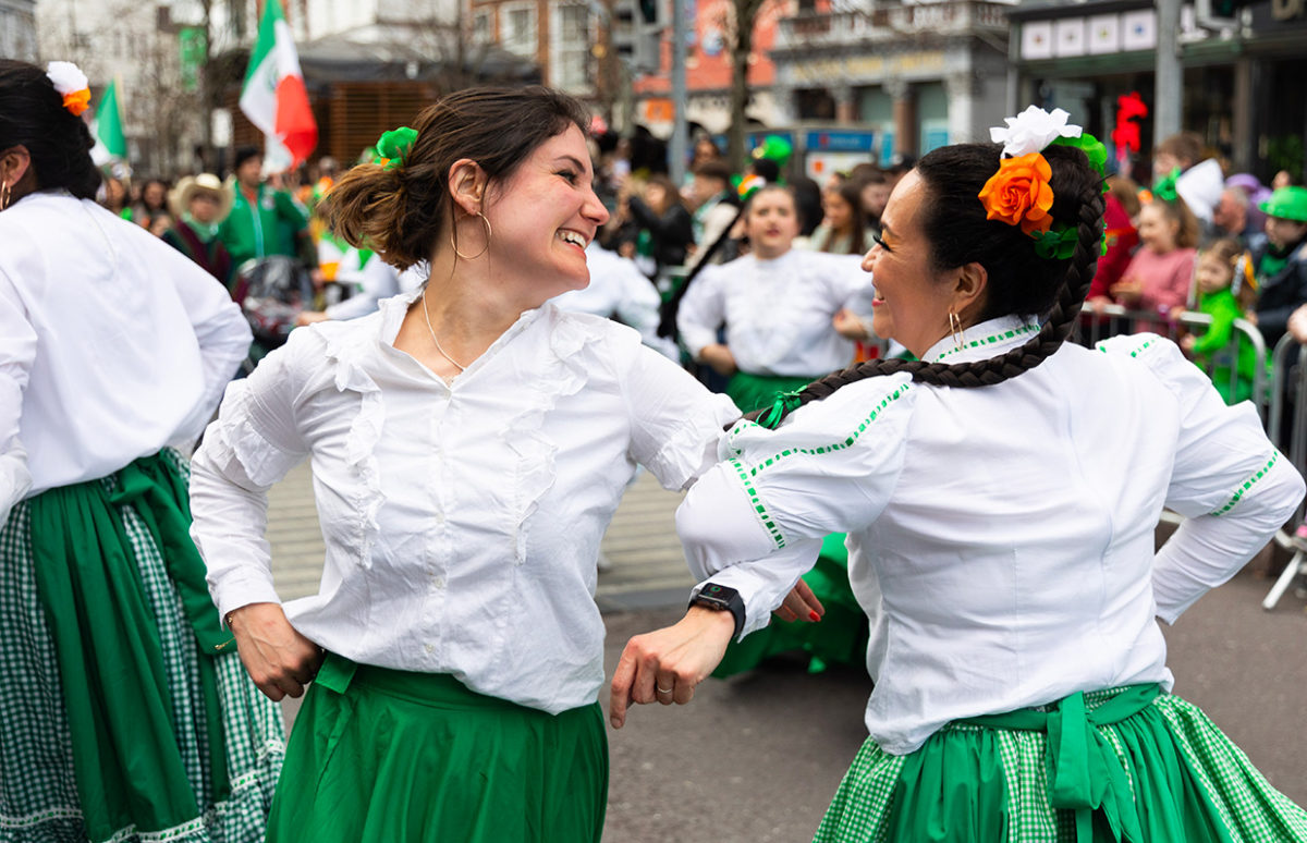 Women in white, orange and green dancing at a St Patrick's Festival in Cork, Ireland.