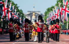 A military band marching down the Mall in London with Buckingham Palace in the background and Union Jacks.