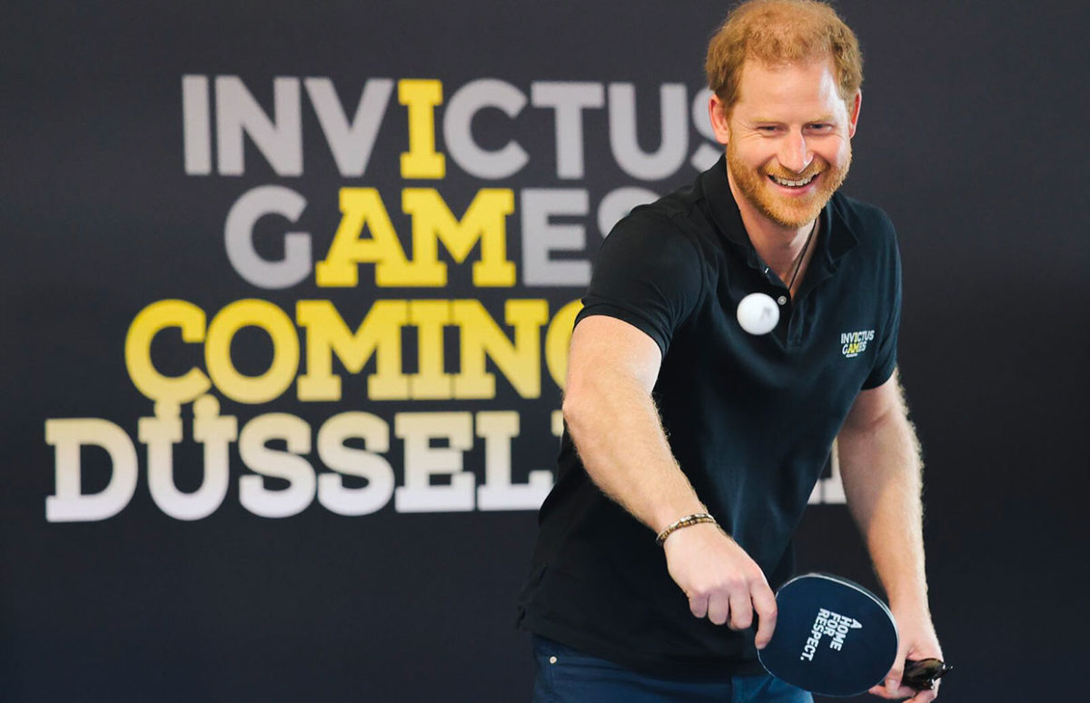 Prince Harry playing table tennis in front of a sign saying Invictus Games Coming to Düsseldorf
