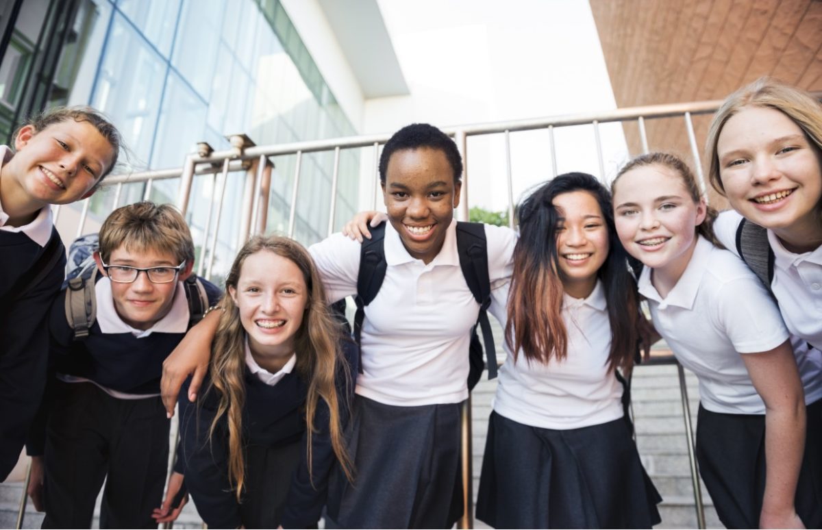 A group of secondary-age pupils in a neutral white and grey uniform crowded together and looking at the camera.