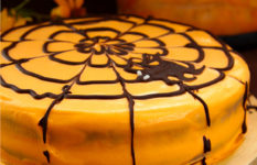A Halloween cake with orange icing and a spider's web.