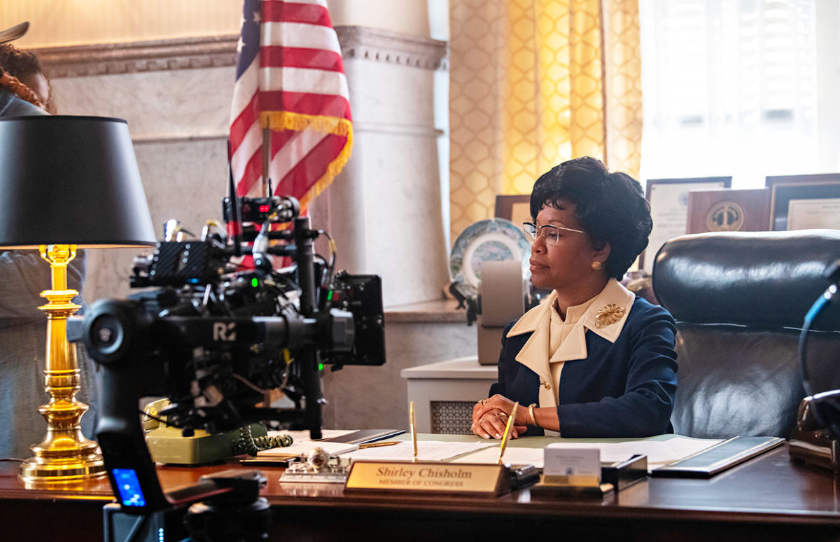 Regina King as Shirley Chisholm, being filmed at a desk with an American flag in the background.