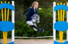 A girl on a toy horse (hobby horse) jumping over an obstacle.