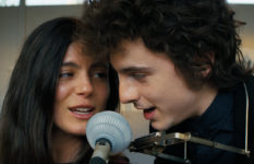 Monica Barbaro as Joan Baez and Timothée Chalamet as Bob Dylan, sharing a mike.