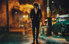 Timothée Chalamet as Bob Dylan, walking down a street dressed in black.