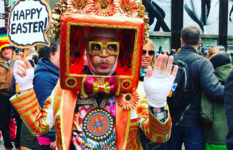 A man in an elaborate costume and a Happy Easter sign poses for the crowd on Fifth Avenue, NYC, during the Easter Bonnet Parade.