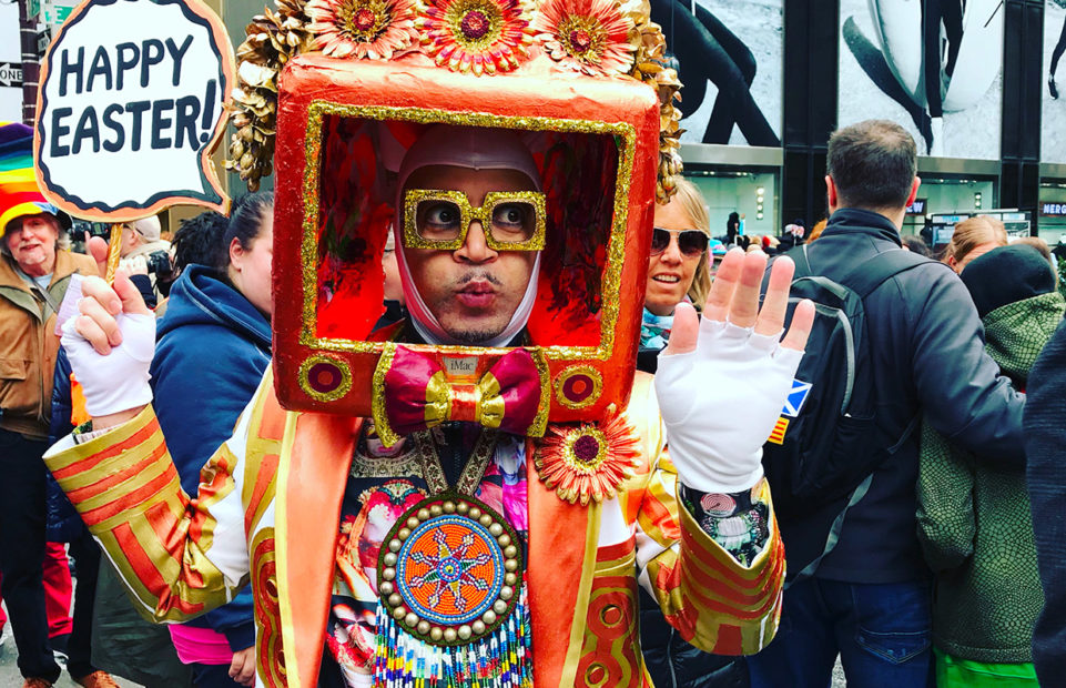 A man in an elaborate costume and a Happy Easter sign poses for the crowd on Fifth Avenue, NYC, during the Easter Bonnet Parade.