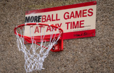 A sign where More has replaced No in front of "ball games at any time", and a basketball hoop attached.
