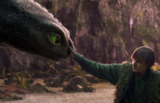 The character Hiccup reaching out to touch his dragon on the snout.