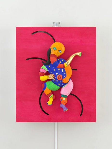 A brightly coloured sculpture of the Indian elephant god Ganesh on a magenta-coloured wall.